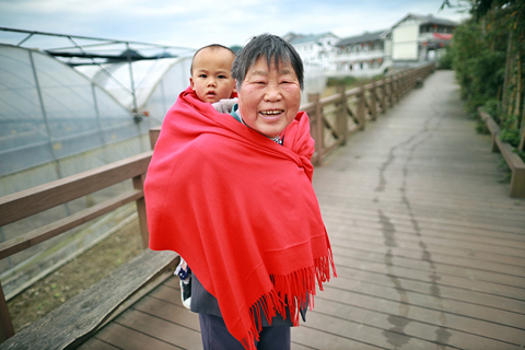 ◎ 本月十三日,一位花茂村村民背著孩子在村裡散步。(新華社記者劉續 攝)